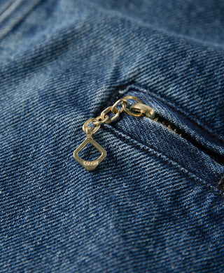 Gold-tone zipper pull with small tag on indigo denim jacket