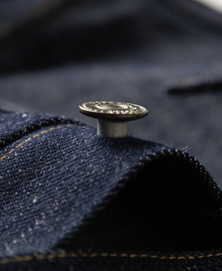 Indigo denim jacket close-up of metal button on fabric seam