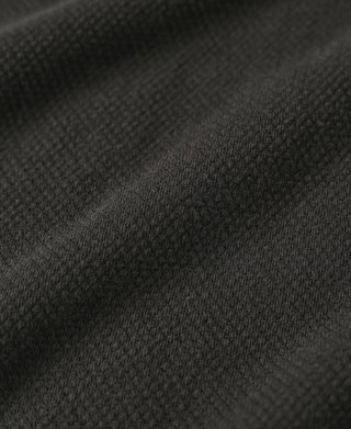 Black waffle-knit fabric texture close-up, fine woven pattern