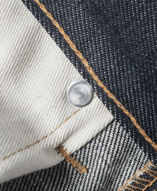 Indigo denim jeans hem with tan selvedge edge, off-white facing, and silver button