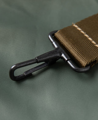 Black metal zipper pull and brown strap hardware on sage green helmet bag