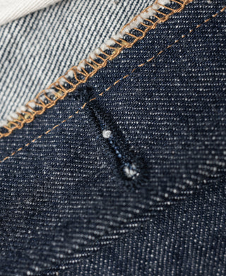 Denim jeans close-up of selvedge-style edge stitching with small speckled texture.