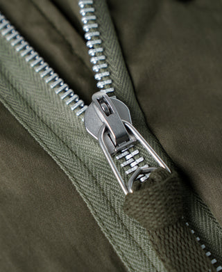 Olive parka front zipper with metal pull and teeth; close-up