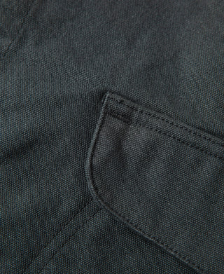 Dark green canvas vest close-up of pocket edge seam and curved stitch detailing