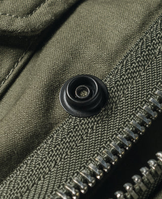 Olive field jacket cuff button with textured fabric and zipper teeth close-up