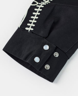 Black jacket cuff with cream embroidered trim and two snap fasteners