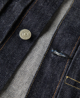 Indigo denim jacket front yoke with metal button and contrast gold topstitching.