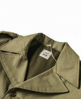 Olive field jacket with button placket and inner size label at open collar
