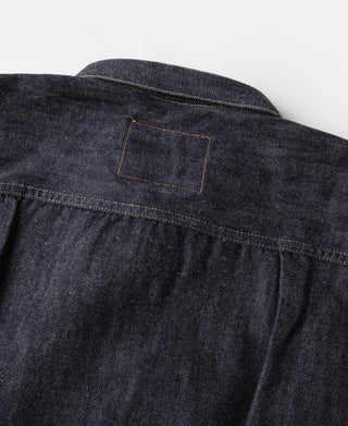 Indigo denim jacket back yoke seam with small rectangular patch detail.