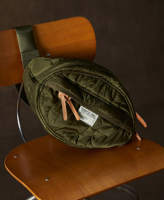 Olive waist bag with top zip, curved shape, and tan leather accents, angled view