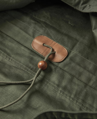 Olive cotton parka pocket flap with brown leather tab and drawstring