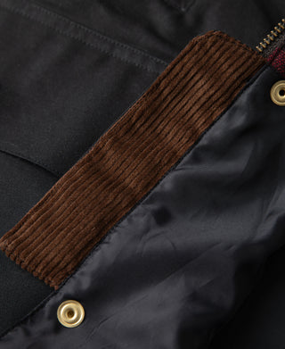 Brown ribbed corduroy sleeve cuff with brass snap on black jacket