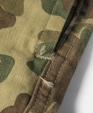 Camouflage cotton pants, close-up of cuff stitching and buttoned strap detail.