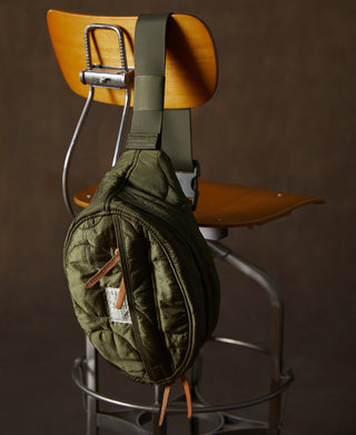 Olive waist bag with adjustable webbing strap, metal buckle, and tan leather pull tabs