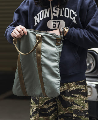 Sage green canvas helmet bag with front handle and zipper, camo side panels