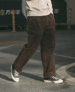 Brown corduroy trousers on model, relaxed straight legs, side pockets, cuffed hem