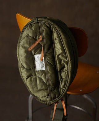Olive waist bag side view with front pocket, hanging tag, and tan leather zipper pull