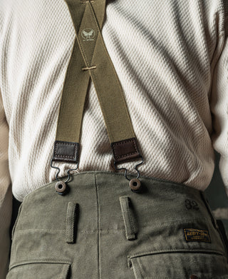 Olive suspenders with dark leather straps and metal button rings at waist