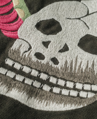 Gray embroidered skull patch with stitched details on dark gray-green jacket