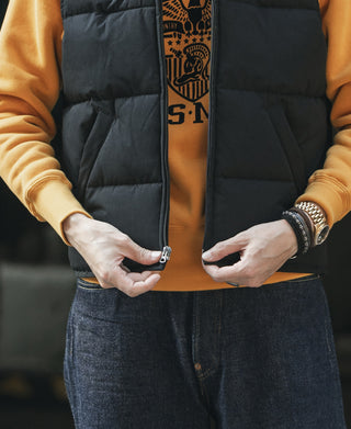 Black quilted vest with zipper partially open, hands pulling the front.