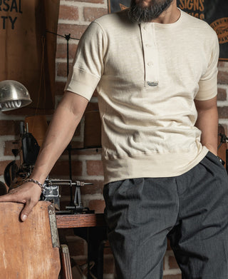Cream henley T-shirt with short sleeves and button placket, worn with dark pants