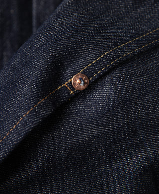 Indigo denim jacket corner detail with copper-tone snap and orange-stitched seam