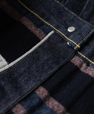 Indigo denim jacket interior seam with plaid blanket lining and metal snap button