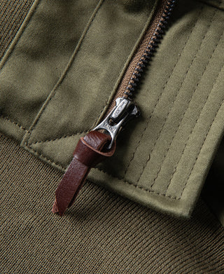 Olive flight jacket front zipper with metal pull and stitched pocket panel.