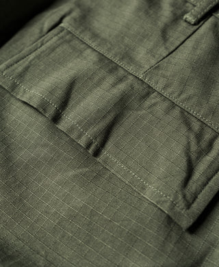 Olive fatigue pants with stitched cargo pocket flap and pleated front, close-up