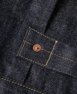 Indigo denim jacket interior corner tag with copper button and gold topstitching.
