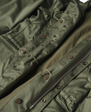 Olive field jacket front with button placket, waist tabs, and zipper, angled view