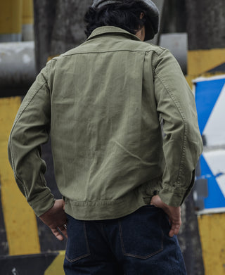 Olive fatigue jacket worn by model, back panel with button front hem tabs