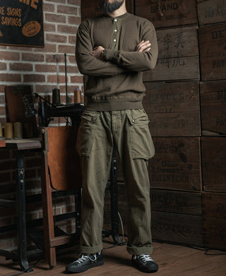 Man standing in an olive-brown ribbed long-sleeve henley shirt with button placket