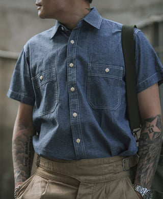 Blue chambray short-sleeve work shirt on model, button front, chest pockets, pointed collar
