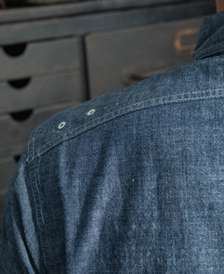Blue chambray shirt back shoulder with buttoned vent and stitched seam detail.