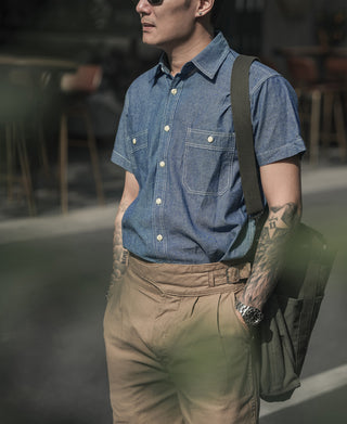 Blue chambray work shirt on model, short sleeves, chest pockets, button-down collar
