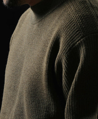 Olive wool sweater shoulder and upper sleeve detail, textured knit pattern.