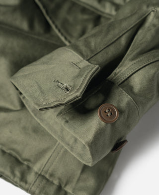Olive field jacket cuff with brown button and reinforced pocket corner, close-up
