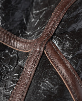 Dark brown leather flight jacket seam with cream shearling trim along the edge