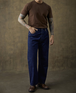 Men's coffee-brown crewneck cotton T-shirt with dark blue jeans and tattooed arms