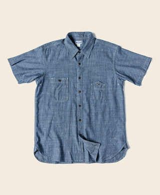 Blue chambray work shirt, short-sleeve button-up with pointed collar and chest pockets.