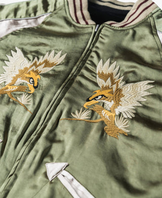 Close-up of green reversible jacket with bird embroidery, zipper, and contrast trim