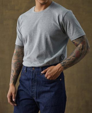 Gray cotton tubular T-shirt and dark blue jeans, male model standing with hand in pocket.