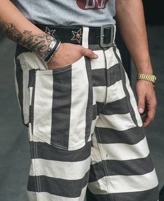 Wide striped prisoner pants with side pockets, white and black stripes, worn with black belt.