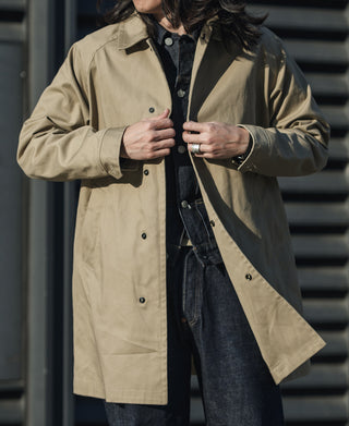 Khaki all-weather trench coat on model, front buttons and blue-trim lining detail