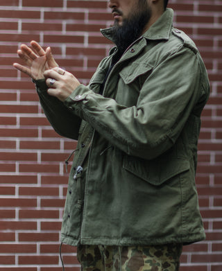 Olive field jacket worn with flap pockets and snap front over camouflage pants
