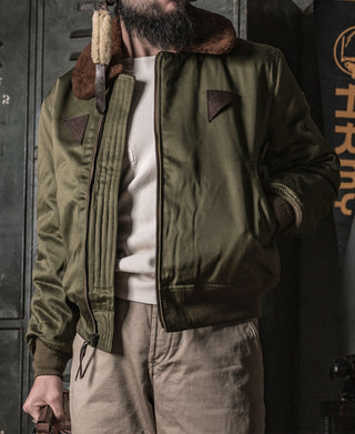 Olive flight jacket worn by model with stand collar and front zip.