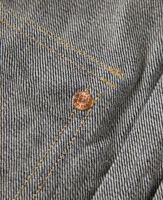 Indigo denim jacket cuff close-up with copper snap button and gold topstitching.