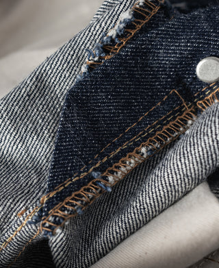 Dark blue denim pocket corner with visible chainstitch and orange-brown topstitching