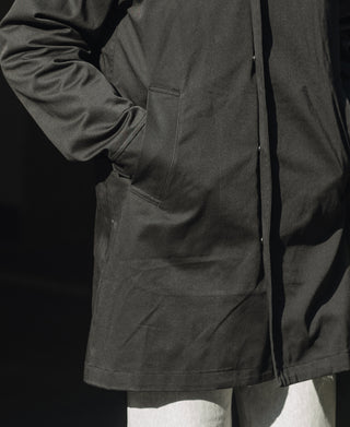 Black all-weather trench coat, side view with flap pocket and zip front